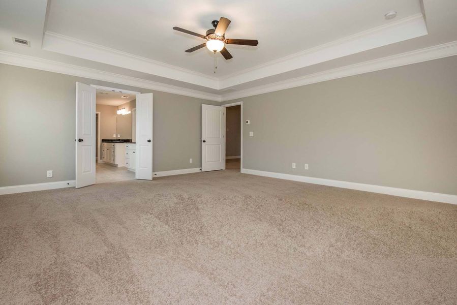 Spacious bedroom with beige carpet, gray walls, white trim, and doors leading to a bathroom.