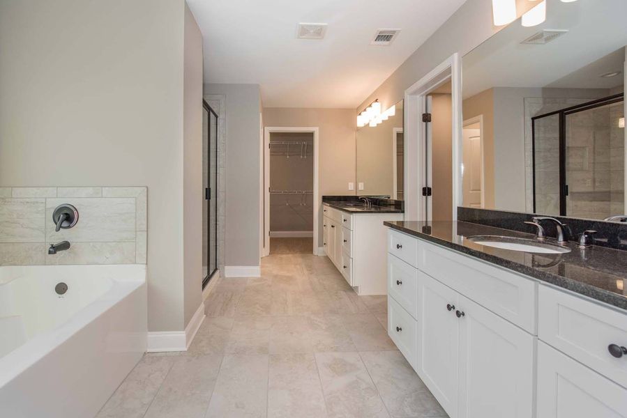 Spacious bathroom with white cabinets, black countertops, walk-in shower, and bathtub; neutral colors.