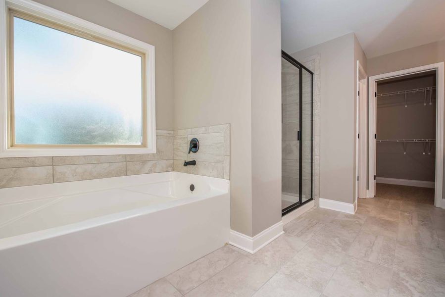 Bathroom with a white bathtub, shower, and walk-in closet. Gray walls and flooring.