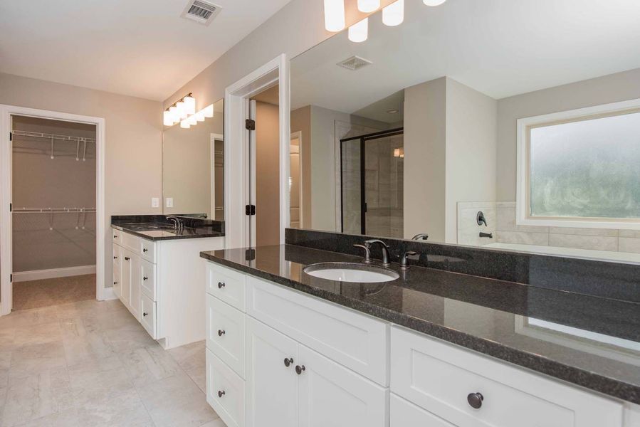 Spacious white bathroom with double vanity, dark countertops, and walk-in closet.