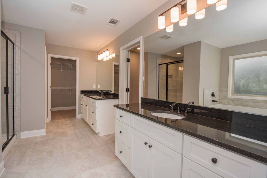Spacious modern bathroom with white cabinets, black countertops, and a walk-in closet.