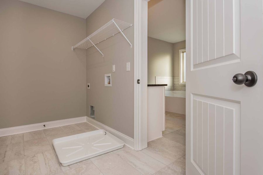 Empty laundry room with neutral walls, white wire shelving, and open door to a second room.