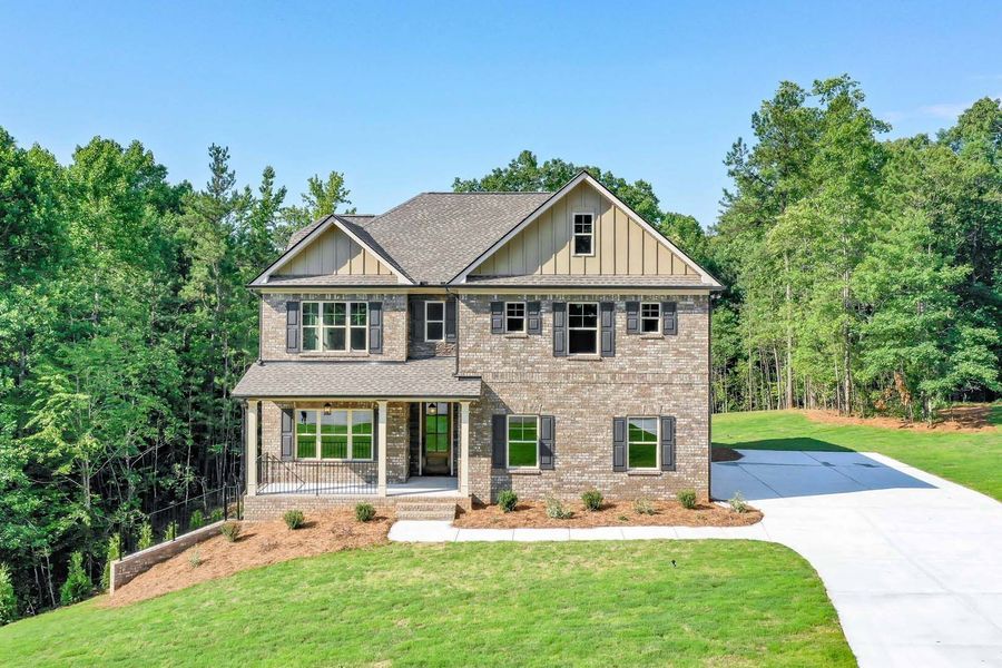 Two-story brick house with gray shutters and roof, green lawn, and trees under a blue sky.