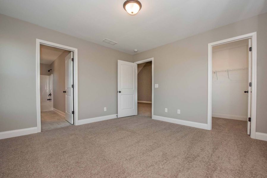 Empty bedroom with beige carpet, gray walls, and three white doorways.