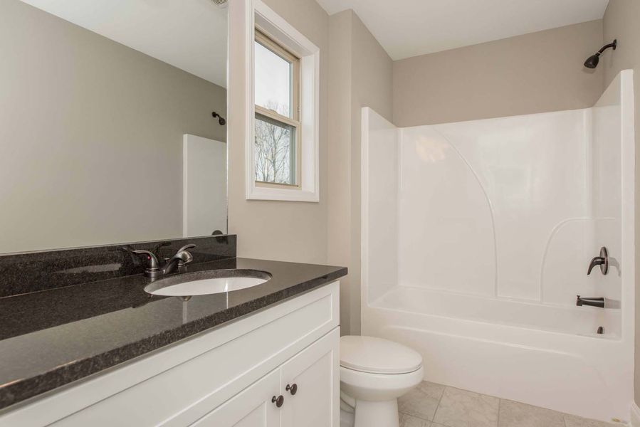 Bathroom with white vanity, tub, and toilet, and dark countertop. Gray walls, small window.