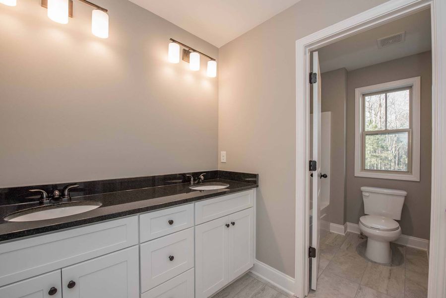 Bathroom with white cabinets, black countertop, and a separate toilet room.