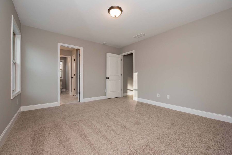 Empty bedroom with gray walls, beige carpet, white trim and doors, and a ceiling light.