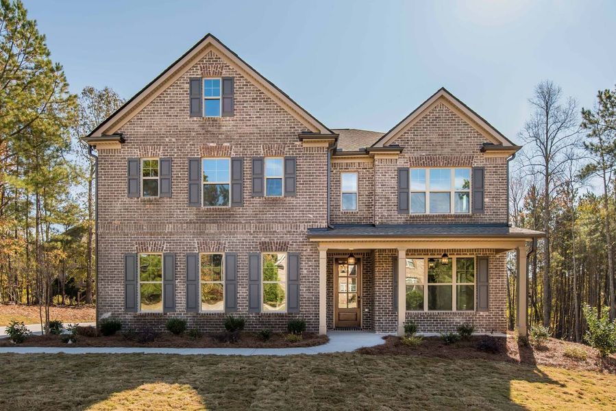 Two-story brick house with shutters and porch on a sunny day.