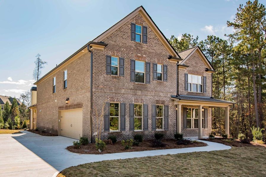 Two-story brick house with a porch, garage, and driveway on a sunny day.