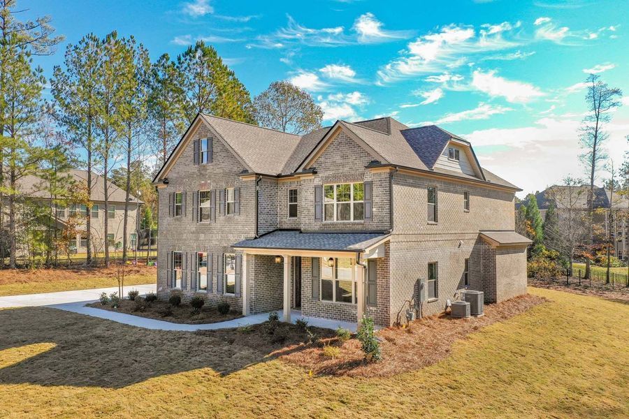 Two-story brick house with a covered porch on a grassy lot under a cloudy blue sky.