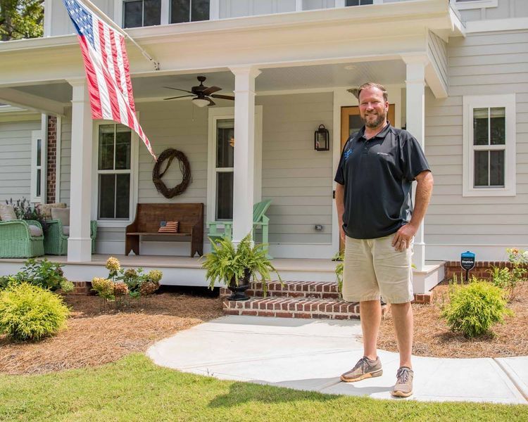 Man standing on a sidewalk in front of a house with an American flag.