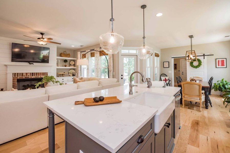Open-concept kitchen with white island, pendant lights, and view of living area with fireplace and seating.