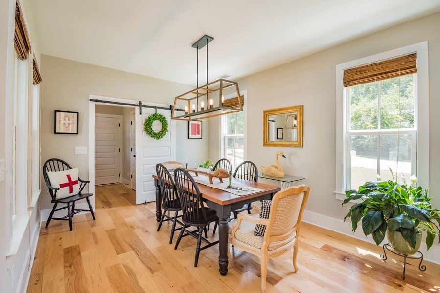 Dining room with wooden table and chairs, hardwood floor, and large windows.