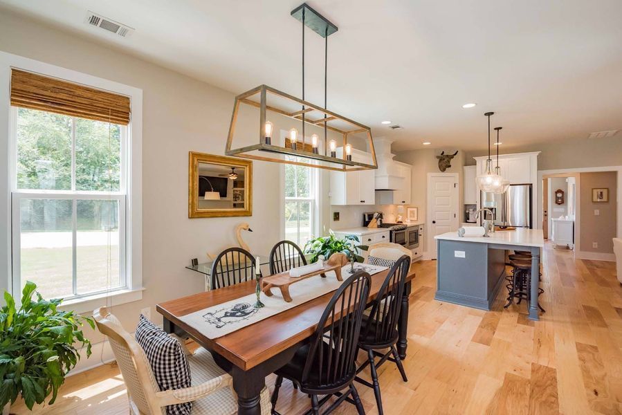 Open-plan dining area with wooden floors, dark table, six chairs, a chandelier, and a view of the kitchen.