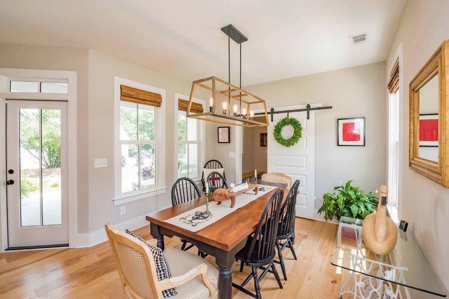 Dining room with wooden table, six chairs, rustic light fixture, sliding barn door, and greenery.