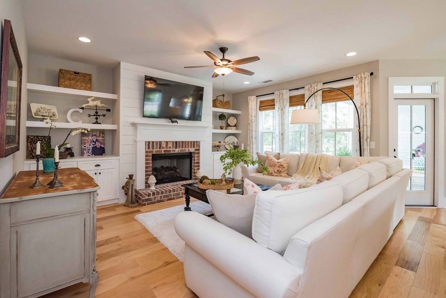 Cozy living room with white sectional sofa, fireplace, shelves, and hardwood floors.