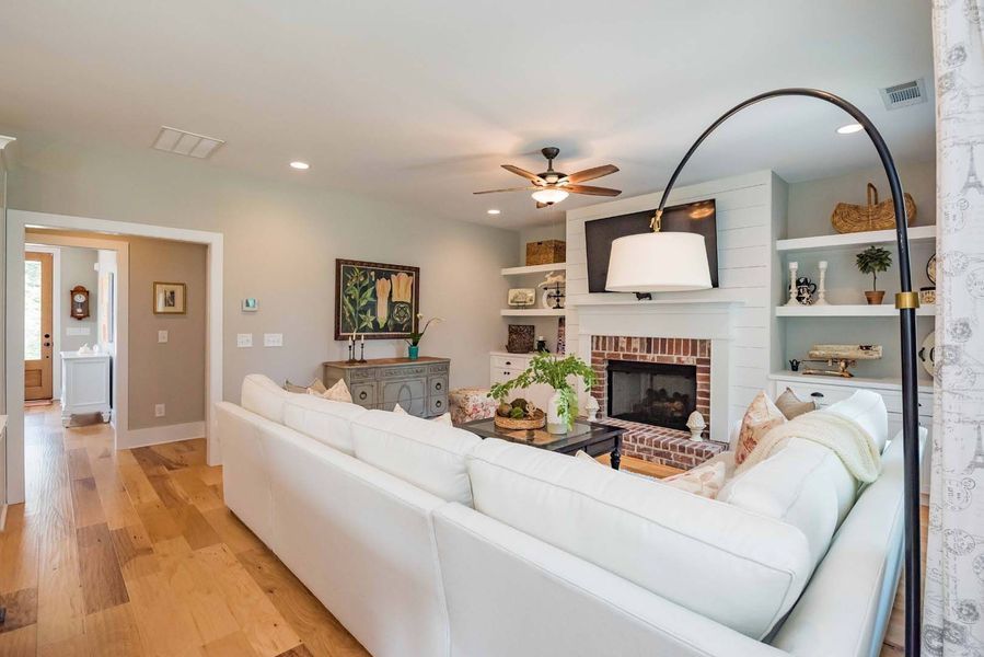 Spacious living room with white sofa, brick fireplace, hardwood floors, and an arched floor lamp.