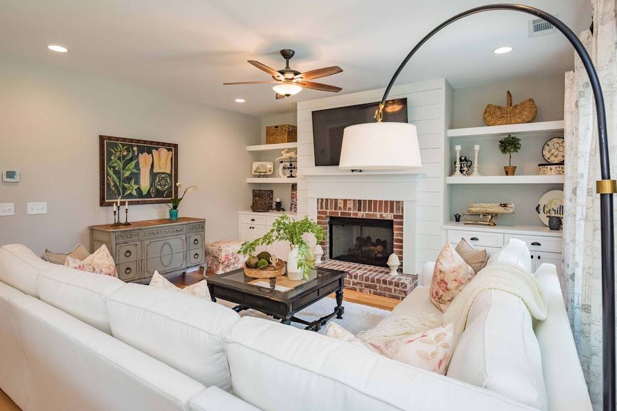 Cozy living room with white sofa, fireplace, and built-in shelves. Neutral colors, natural light, and a ceiling fan.