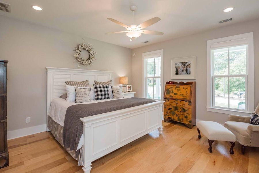 Bedroom with white bed, wooden floors, windows, and a vintage cabinet.
