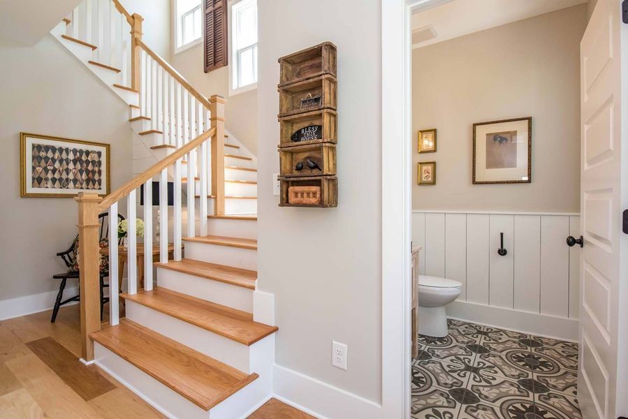 A stairway and a powder room. Oak stairs, white railing, and beige walls. Powder room has a patterned floor