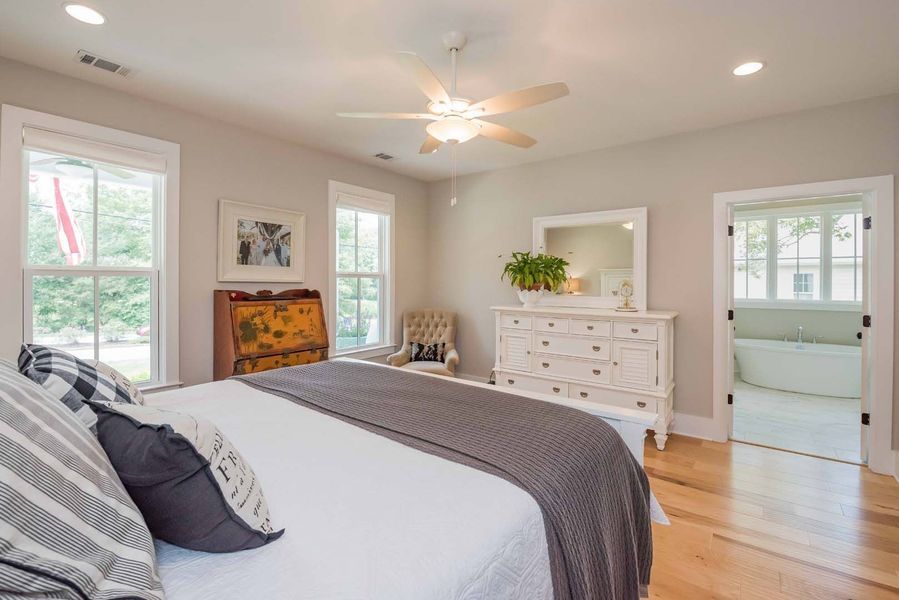 Bedroom with a bed, dresser, windows, and a doorway to a bathroom; light, neutral colors.
