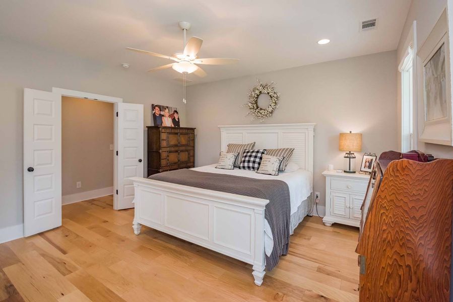 Bedroom with white bed, hardwood floors, and wooden dresser.