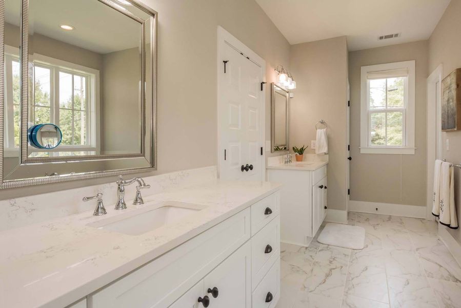 Bathroom with white cabinets, marble floor, and large mirror.