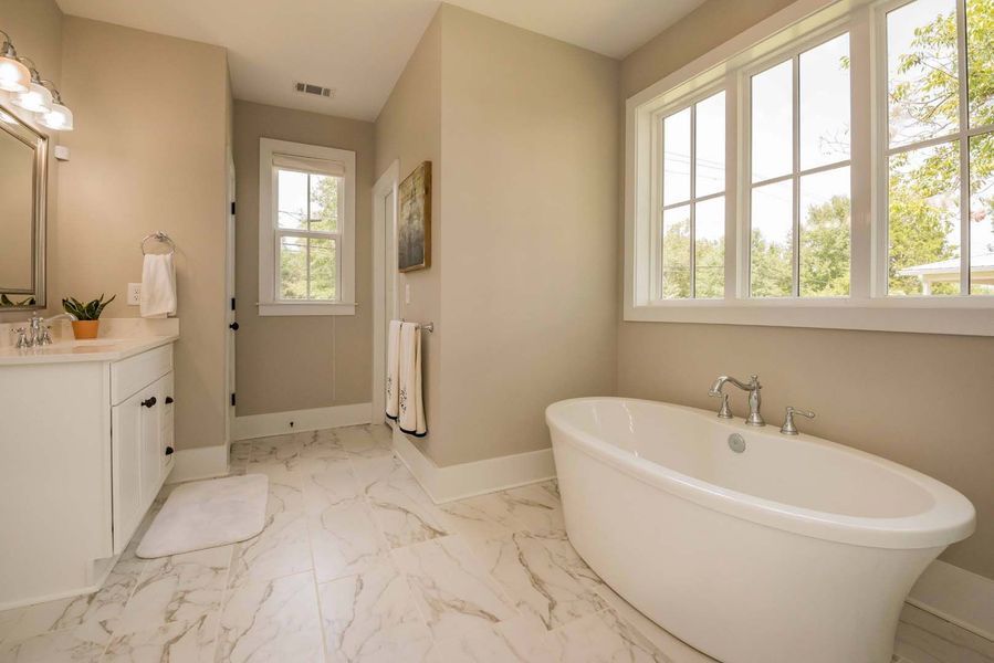 Bright, airy bathroom with a white tub, large windows, and marble floors.