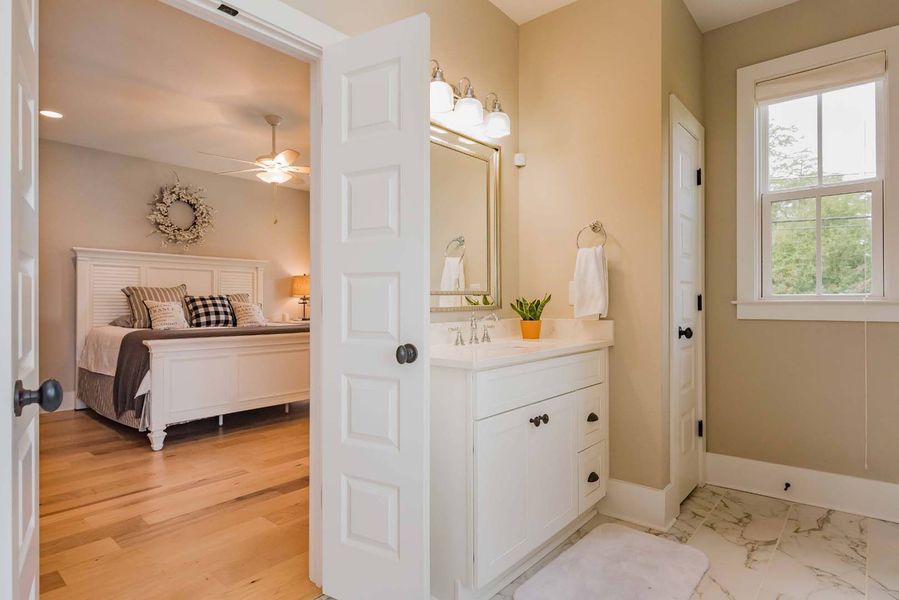 Bedroom doorway leading to a bathroom. Bedroom has white bed, the bathroom has a vanity.