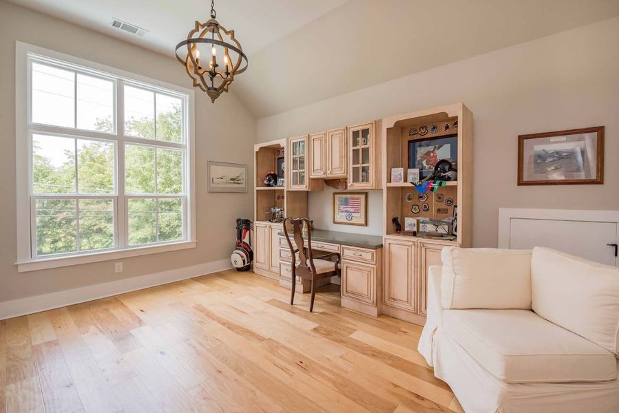 Home office with wood floors, built-in desk, white walls, large window, and cream-colored furnishings.