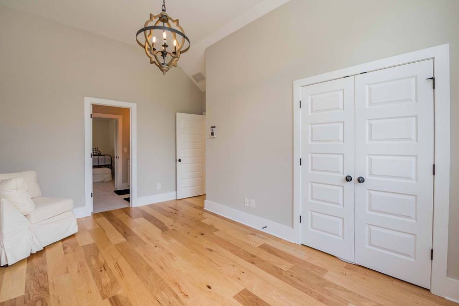 Empty room with light wood floors, white doors, and a chandelier. A white chair sits in a corner.