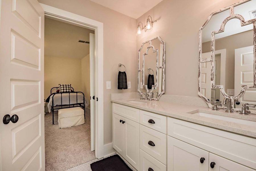 Bathroom with white vanity, ornate mirrors, and doorway to a bedroom with a bed.