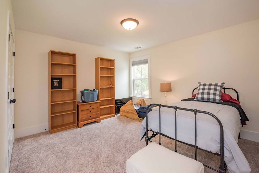 Bedroom with beige walls, carpet, and furniture including a bed, bookshelves, and dresser.