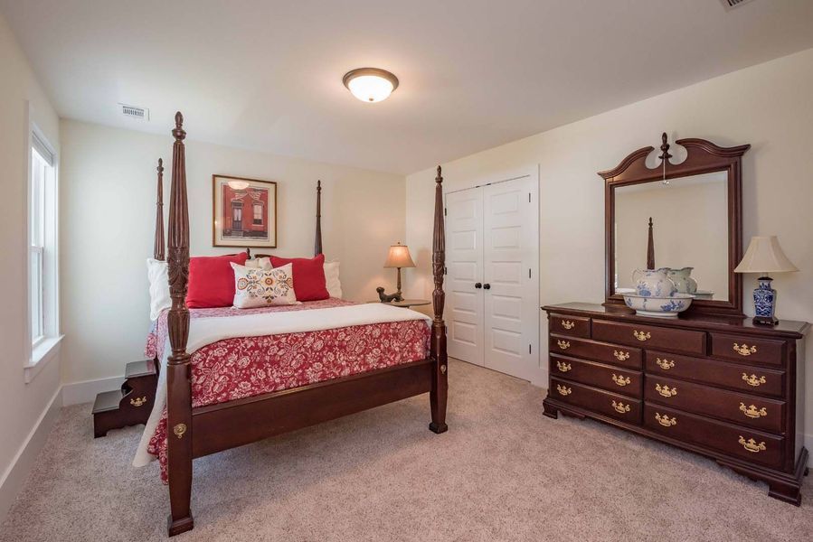 Bedroom with a four-poster bed, dark wood dresser, and neutral carpet. Red and white bedding.