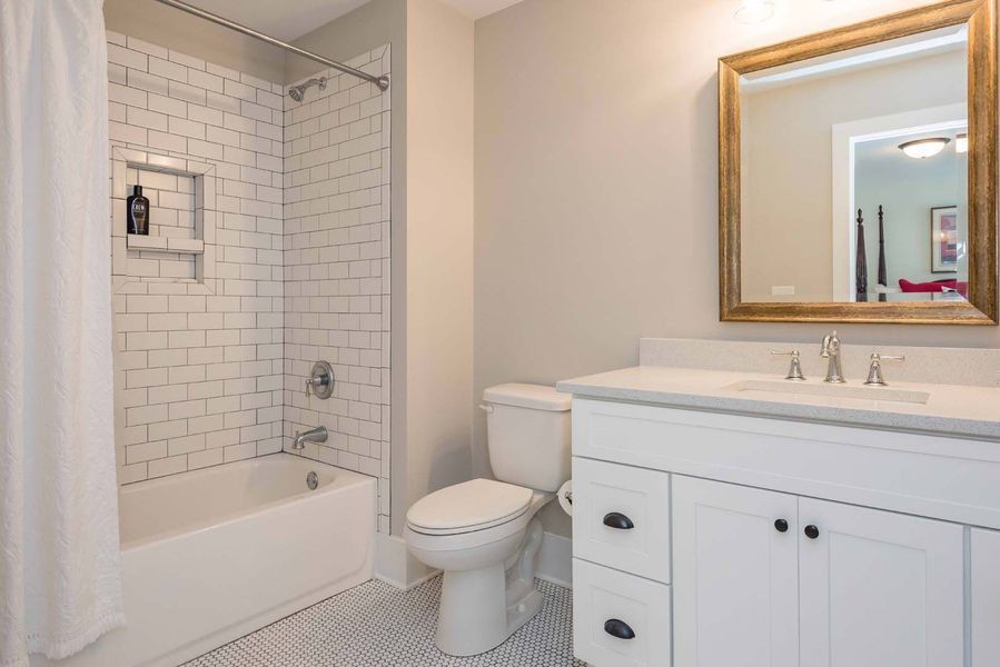 White bathroom with a bathtub, toilet, vanity, and gold-framed mirror.