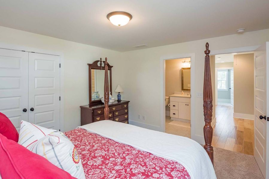 Bedroom with a four-poster bed, dresser, and bathroom entrance. Soft colors, warm lighting.