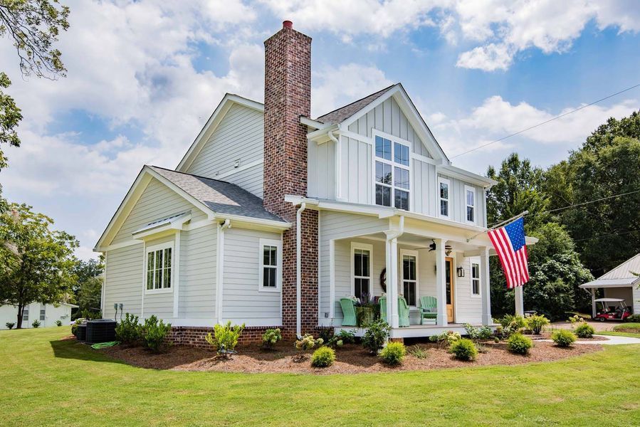 Two-story white house with brick chimney and American flag, sunny day, green lawn.