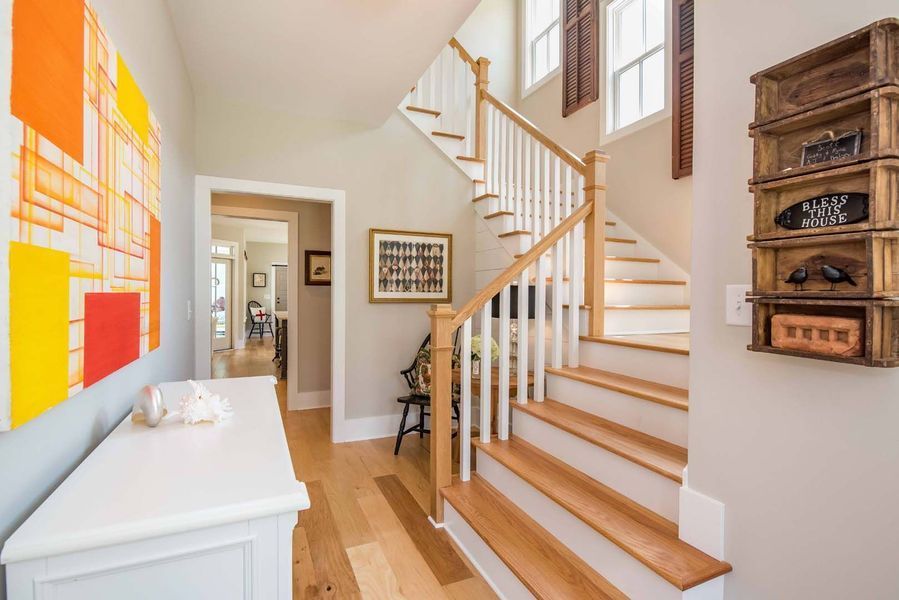 Hallway with staircase, white console table, and colorful artwork. Light wood floors, neutral walls.