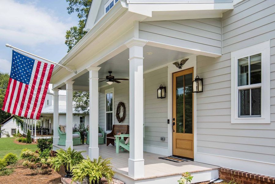 A light-colored house with a porch, American flag, and a wooden door.