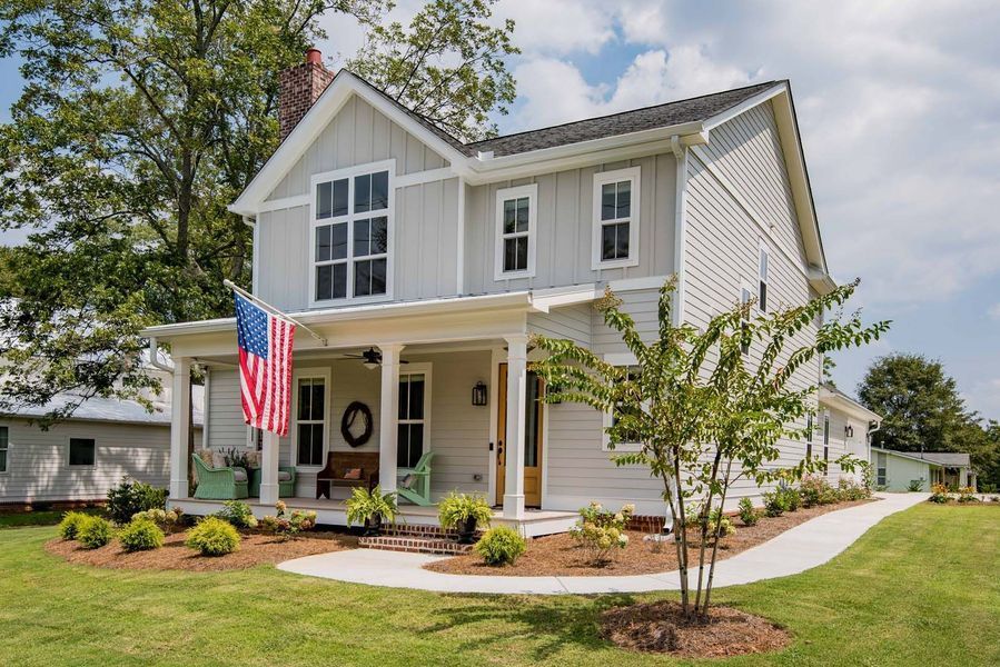 Two-story farmhouse with an American flag on the porch. Light gray exterior, white trim, green lawn.