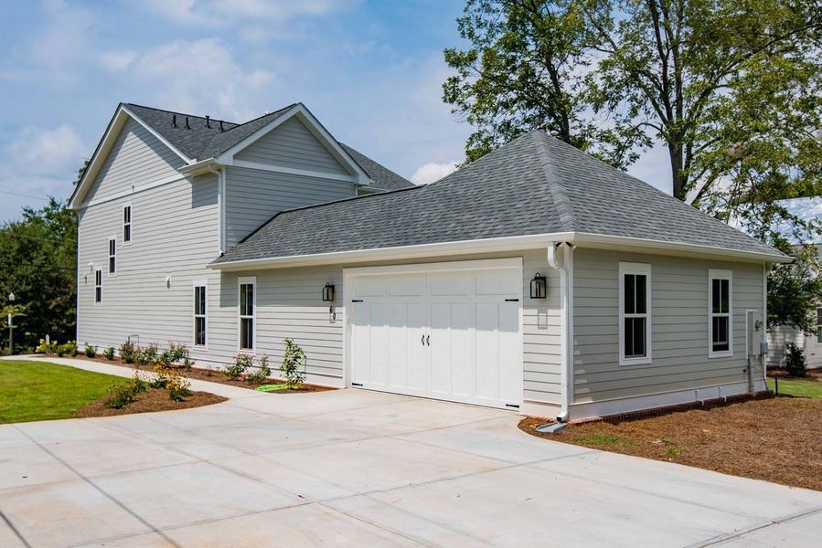 Light gray house with attached garage, white doors, and concrete driveway under a blue sky.