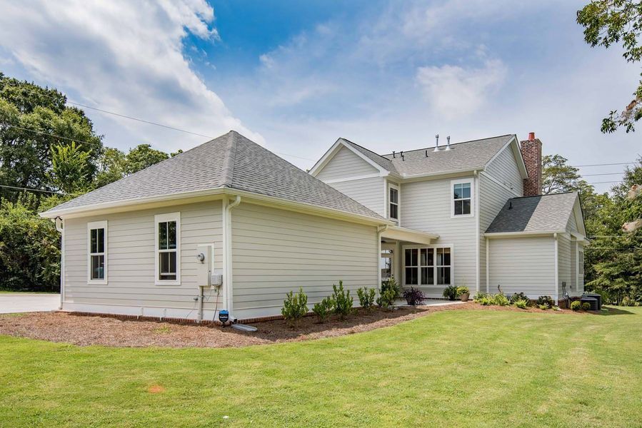 Exterior view of a light gray house with a green lawn and a partly cloudy blue sky.