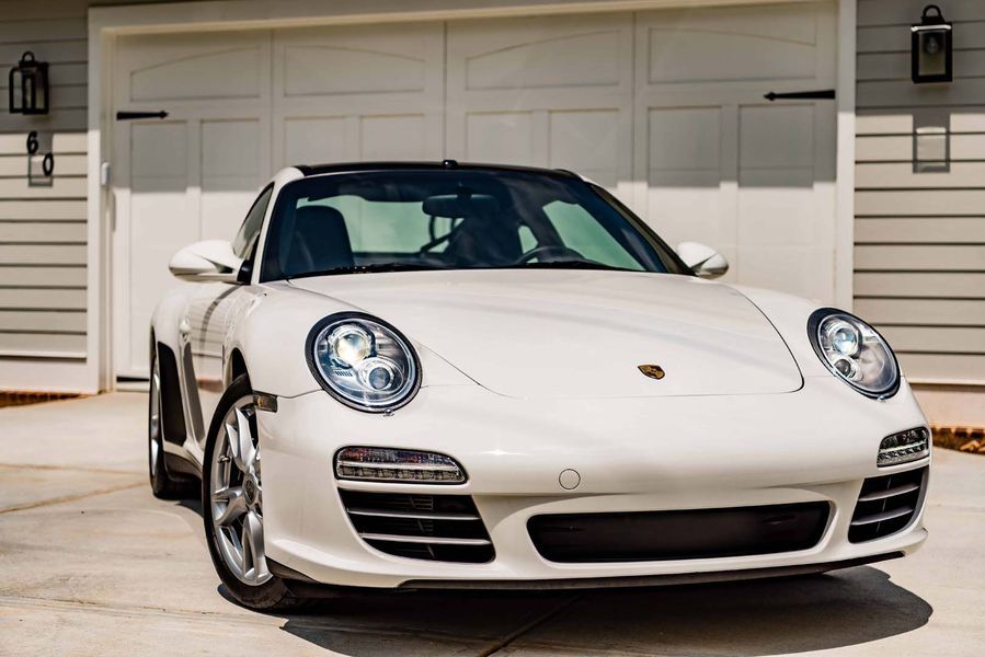 White Porsche sports car parked in front of a garage with white doors.