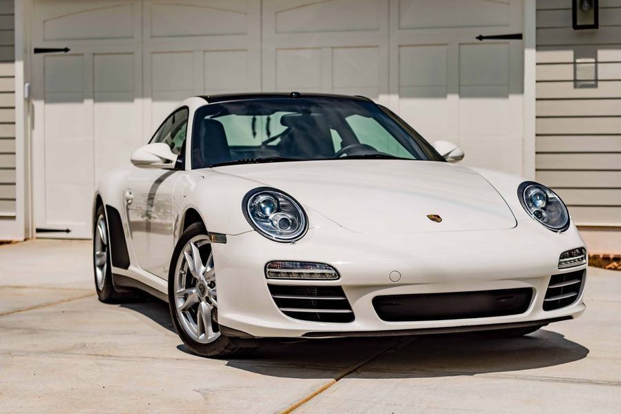 White Porsche 911 parked in front of a garage, sunny day.