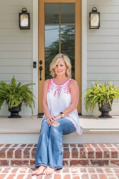Woman seated on brick steps in front of a door, wearing jeans and a white top.