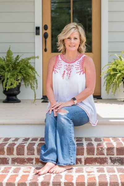 Woman sitting on brick steps in front of a door, wearing white top, jeans, and watch, ferns beside her.