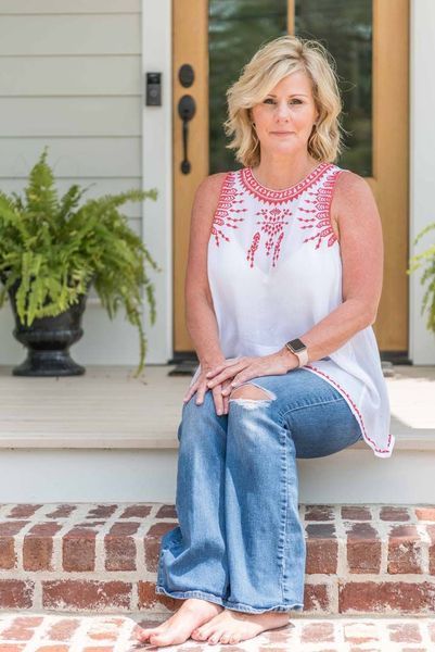 Woman in white top and ripped jeans sits on brick steps in front of a house.