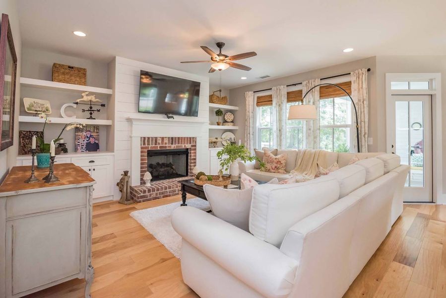 Living room with white sectional sofa, brick fireplace, built-in shelves, and hardwood floors.