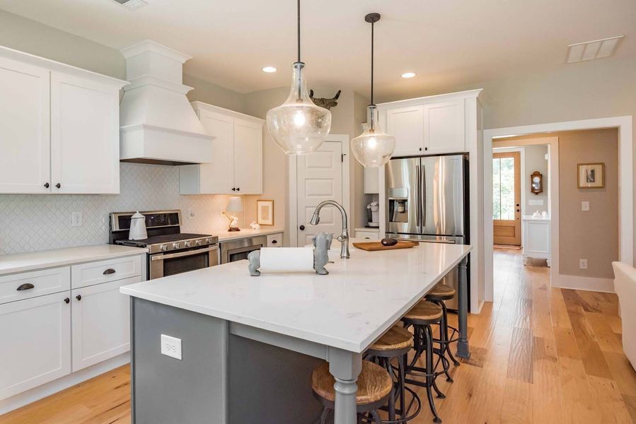 Spacious kitchen with white cabinets, gray island, stainless steel appliances, and wooden floors.