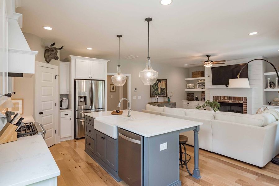Kitchen island with sink and stainless steel appliances, opening to living room with fireplace and white sectional.